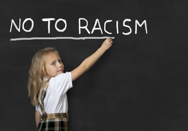 Солодка молодша школярка пише з крейдою ні расизму в шкільному класі дошка — стокове фото