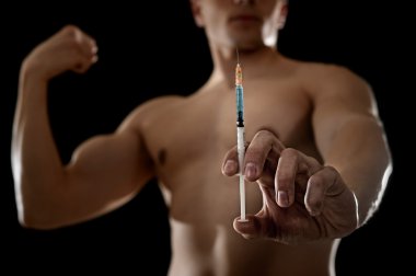 young athletic sportsman holding syringe in sport doping and cheat concept