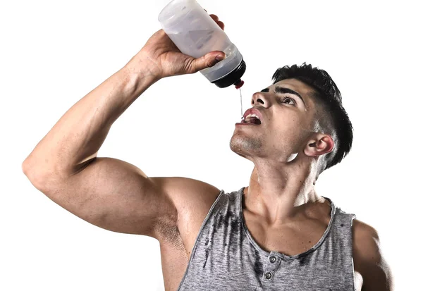 Молодой спортсмен жаждущий питьевой воды держит бутылку льющейся жидкостью на потное лицо — стоковое фото