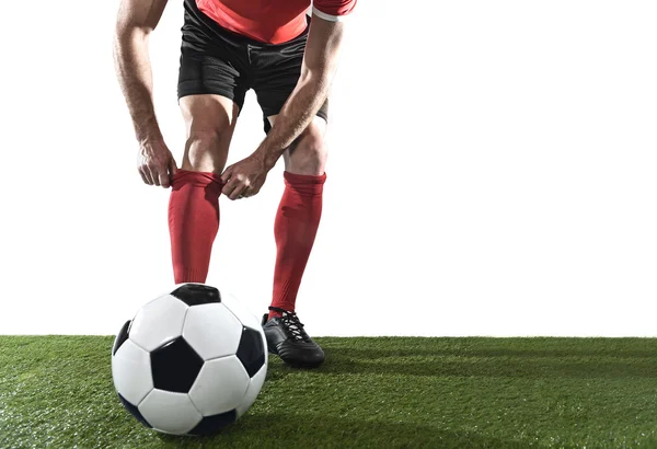 Fotbalist cu mingea purtând pantofi negri ajustând șoseta roșie în picioare pe iarbă verde izolată — Fotografie, imagine de stoc