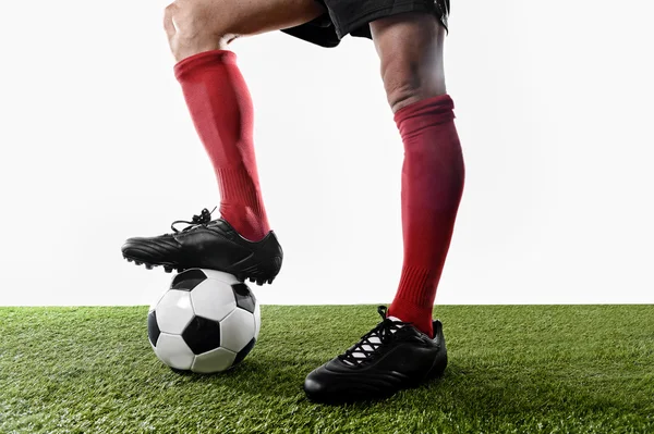 legs feet of football player in red socks and black shoes posing with the ball playing on green grass pitch