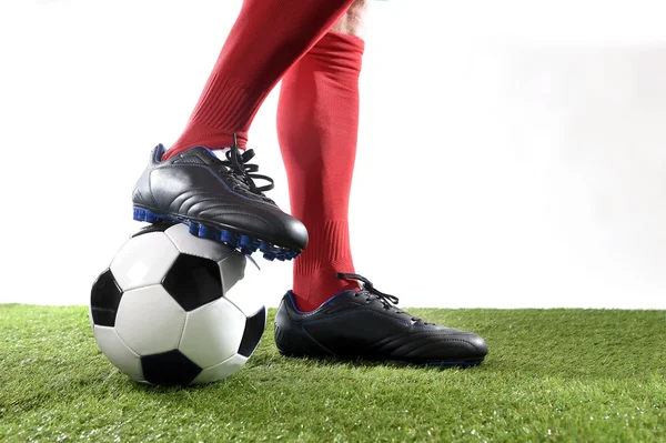 Pernas pés jogador de futebol em meias vermelhas e sapatos pretos posando com a bola jogando no campo de grama verde — Fotografia de Stock
