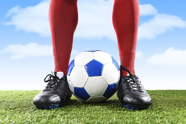 close up legs feet football player in red socks and black shoes playing with ball on grass pitch outdoors