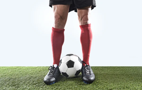 legs feet of football player in red socks and black shoes posing with the ball playing on green grass pitch