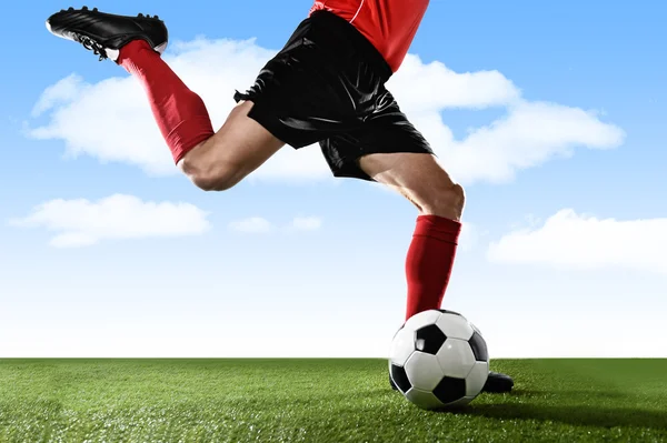 Cerrar las piernas del jugador de fútbol en calcetines rojos y zapatos negros corriendo y pateando la pelota en acción de tiro libre jugando al aire libre —  Fotos de Stock