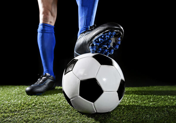 ноги и ноги футболиста в синих носках и черных туфлях, позирующих с мячом, играющим на зеленой траве
