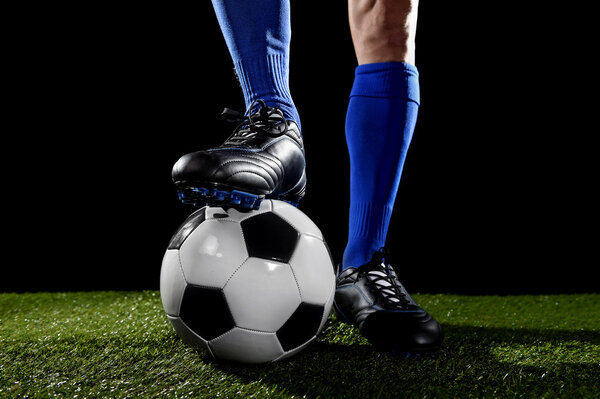 ноги и ноги футболиста в синих носках и черных туфлях, позирующих с мячом, играющим на зеленой траве

