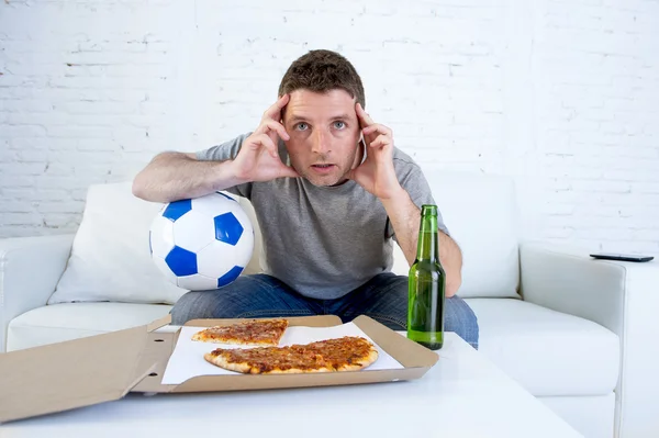 Joven solo sosteniendo la bola y la botella de cerveza viendo el partido de fútbol en la televisión en el sofá en casa sofá — Foto de Stock