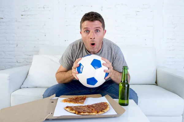 Jovem sozinho segurando bola e garrafa de cerveja assistindo jogo de futebol na televisão em casa sofá — Fotografia de Stock