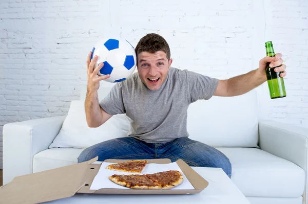 Joven sosteniendo pelota viendo el partido de fútbol en la televisión en el sofá de casa con pizza y cerveza celebrando el gol loco o la victoria —  Fotos de Stock