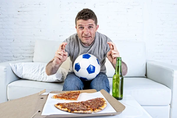 Jonge man alleen in stress kijken naar voetbalwedstrijd op televisie kruising vingers — Stockfoto