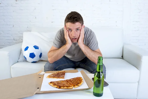 Fan piłki nożnej w stres oglądania meczu piłki nożnej w telewizji w sofa kanapa z pizza box i piwo butelka — Zdjęcie stockowe