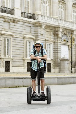 young happy tourist man with backpack riding city tour segway driving happy and excited visiting Madrid palace