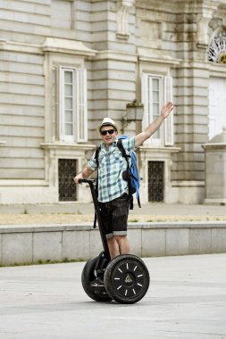 young happy tourist man with backpack riding city tour segway driving happy and excited visiting Madrid palace