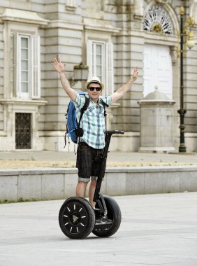 young happy tourist man with backpack riding city tour segway driving happy and excited visiting Madrid palace
