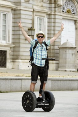 young happy tourist man with backpack riding city tour segway driving happy and excited visiting Madrid palace