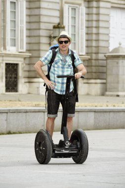young happy tourist man with backpack riding city tour segway driving happy and excited visiting Madrid palace