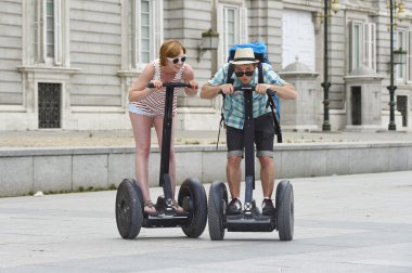 young happy tourist couple riding segway enjoying city tour in Madrid palace in Spain having fun driving together 