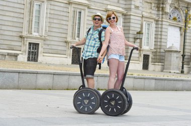 young happy tourist couple riding segway enjoying city tour in Madrid palace in Spain having fun driving together 