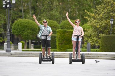 young happy tourist couple riding segway enjoying city tour in Madrid park in Spain together 
