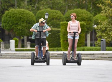 young happy tourist couple riding segway enjoying city tour in Madrid park in Spain together 