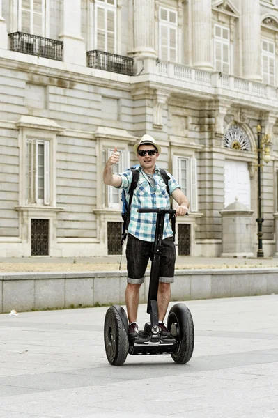 Young happy tourist man with backpack riding city tour segway driving happy and excited visiting Madrid palace — Stock Fotó