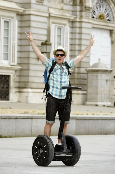 Young happy tourist man with backpack riding city tour segway driving happy and excited visiting Madrid palace — Zdjęcie stockowe