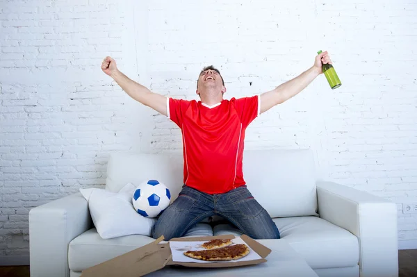 Homem assistindo jogo de futebol na tv em equipe jersey comemorando objetivo louco feliz pulando no sofá — Fotografia de Stock