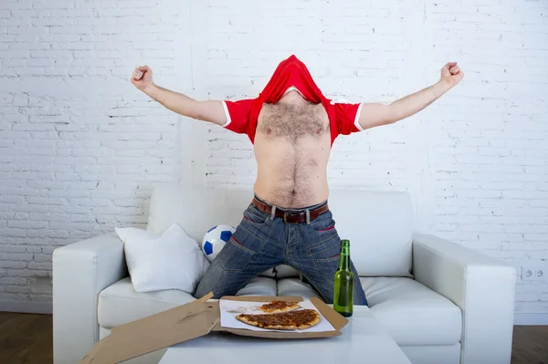 Man watching football game on tv in team jersey celebrating goal crazy happy jumping on sofa — Stock Photo, Image