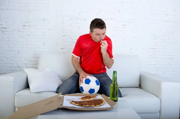 Mies katsomassa jalkapallo peli televisiossa joukkue jersey juhlii tavoite hullu onnellinen hyppäämällä sohvalla — kuvapankkivalokuva
