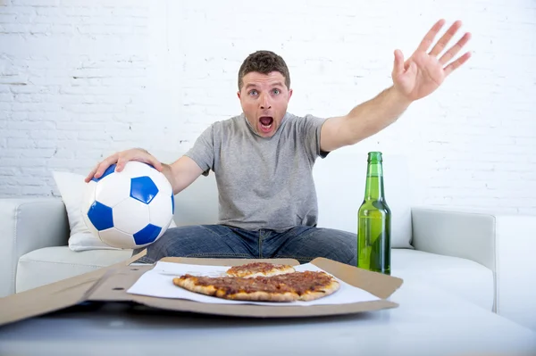 Jovem sozinho segurando bola e garrafa de cerveja assistindo jogo de futebol na televisão em casa sofá — Fotografia de Stock