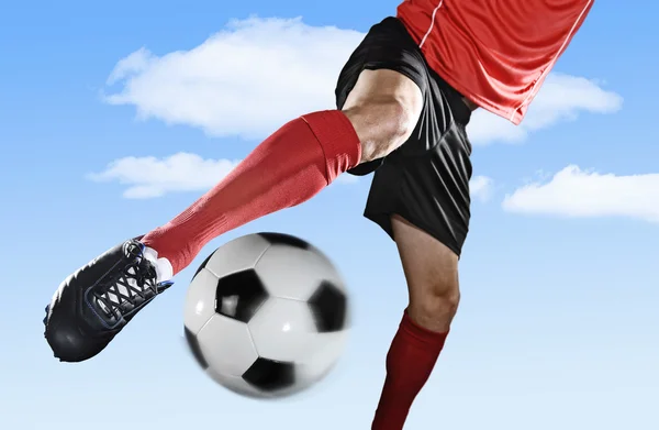 Chiudere le gambe e scarpe da calcio del giocatore di calcio in azione all'aperto calci palla isolata sul cielo blu — Foto Stock