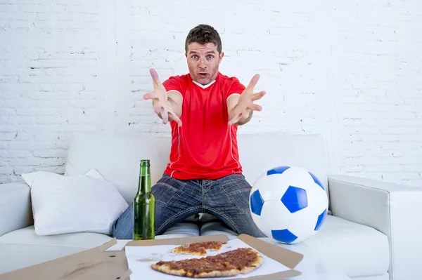 Tifoso di calcio in maglia della squadra a guardare la partita di calcio in TV sul divano di casa gesticolando deluso — Foto Stock