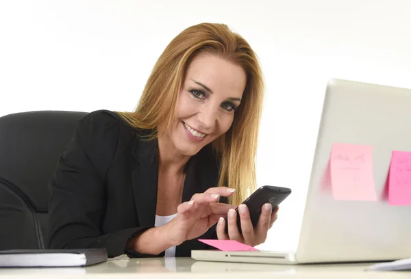 Businesswoman working at laptop computer office desk sending text message on mobile phone — Stock Photo, Image