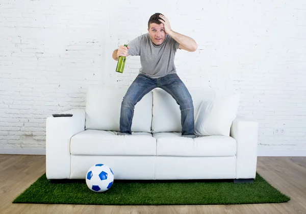 Fan piłki nożnej oglądając mecz telewizyjny na kanapie z trawy boisko dywan w stres — Zdjęcie stockowe
