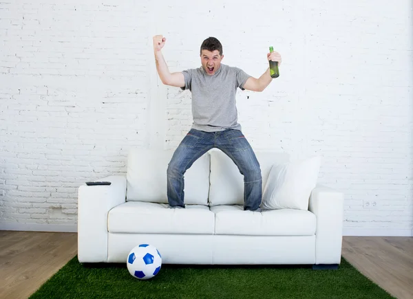 Fanático del fútbol viendo partido de televisión en sofá con alfombra de césped celebrando gol — Foto de Stock