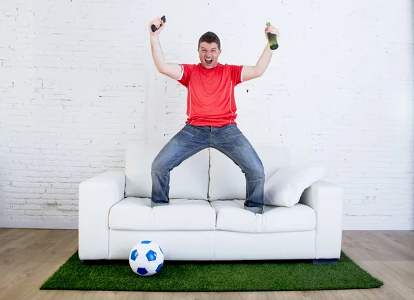 Fã de futebol assistindo tv futebol comemorando gol no sofá no tapete grama emulando campo de estádio — Fotografia de Stock