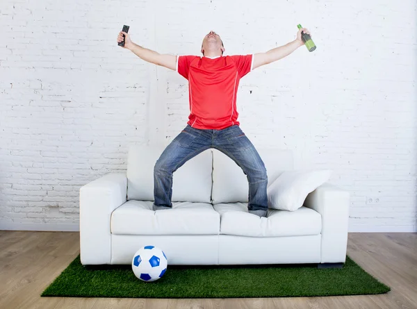 Fanático del fútbol viendo televisión fútbol celebrando gol en sofá en alfombra de hierba emulando campo de estadio — Foto de Stock