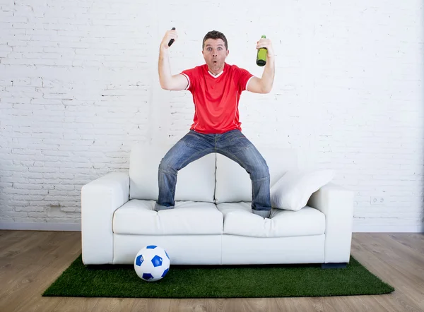 Fã de futebol assistindo tv futebol comemorando gol no sofá no tapete grama emulando campo de estádio — Fotografia de Stock