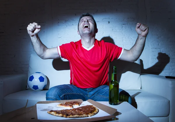 Фанат футбола смотрит футбол по телевизору, празднуя — стоковое фото