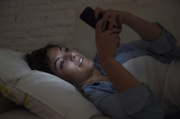 Молодая красивая женщина лежит на домашнем диване, используя мобильный телефон смс улыбаясь счастливой — стоковое фото