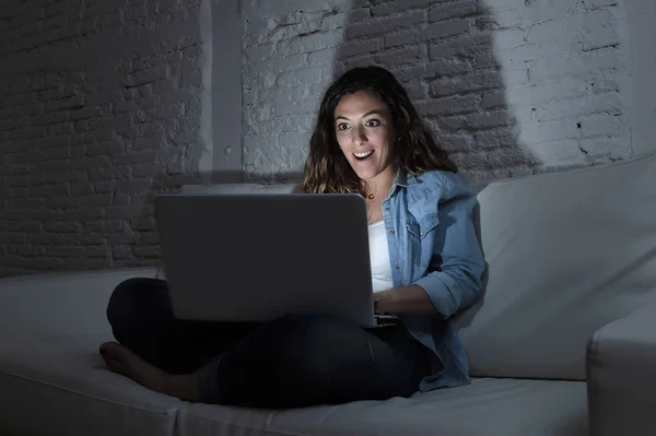 Привлекательная расслабленная женщина дома сидит счастливая на диване с помощью ноутбука в темный вечер — стоковое фото