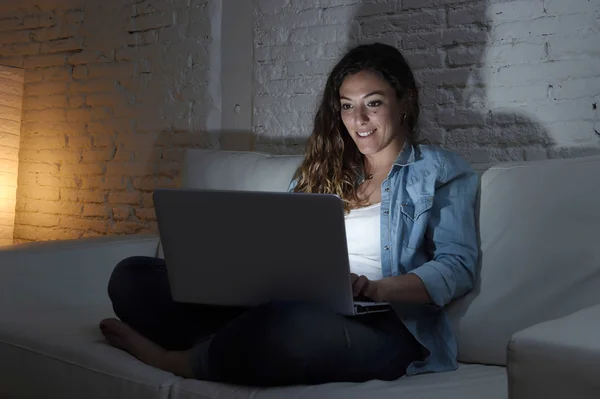Ελκυστική γυναίκα χαλαρή στο σπίτι κάθεται ευτυχισμένος στον καναπέ χρησιμοποιώντας φορητό υπολογιστή τη νύχτα — Φωτογραφία Αρχείου