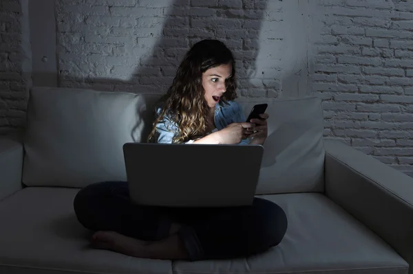 Internet viciada em rede social mulher usando computador portátil e telefone celular no sofá à noite — Fotografia de Stock