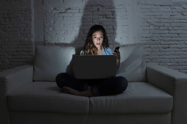 Internet sociala nätverk missbrukare kvinna med bärbar dator och mobiltelefon på soffan på kvällen — Stockfoto