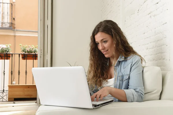 Wanita muda Spanyol yang menarik menggunakan laptop duduk santai bekerja di sofa rumah — Stok Foto