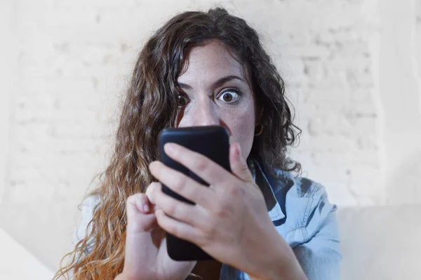 Hispanic woman holding mobile phone in crazy eyes social network and internet addiction concept — Stock Photo, Image