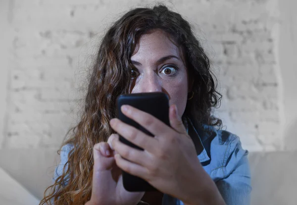 Hispanic woman holding mobile phone in crazy eyes social network and internet addiction concept — Stock Photo, Image