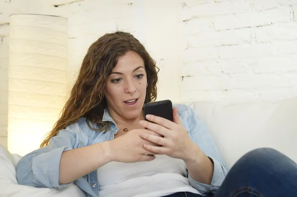 Joven atractiva mujer española usando aplicación de teléfono móvil o mensajes de texto en el sofá de casa — Foto de Stock