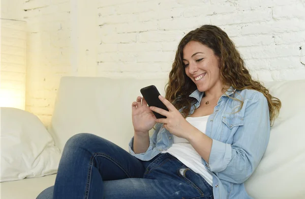 Joven atractiva mujer española usando aplicación de teléfono móvil o mensajes de texto en el sofá de casa —  Fotos de Stock